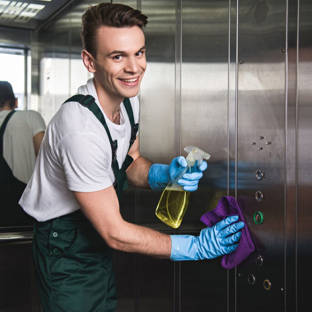 Young cleaning company worker cleaning elevator and smiling at camera