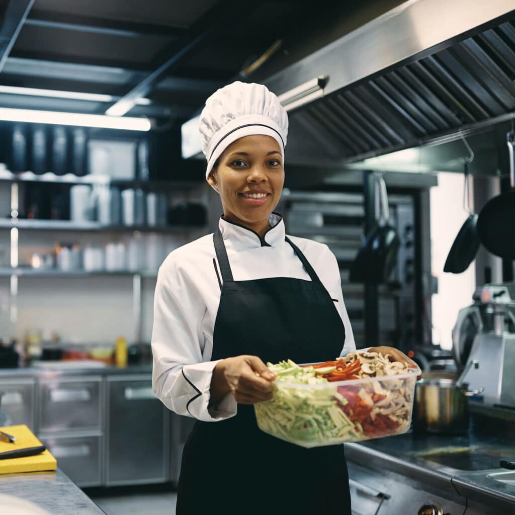 Black female chef preparing food in kitchen at restaurant and looking at camera.