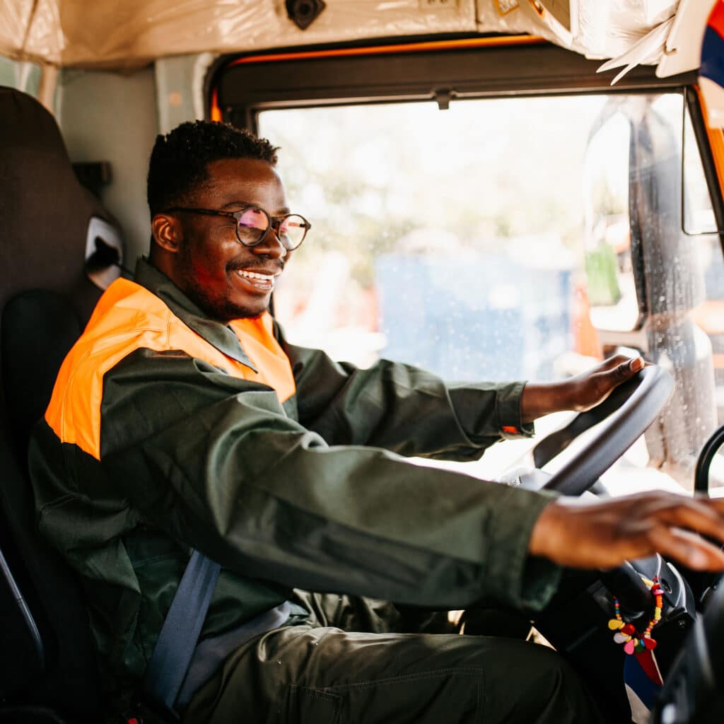 Young African American garbage removal worker driving a waste truck.